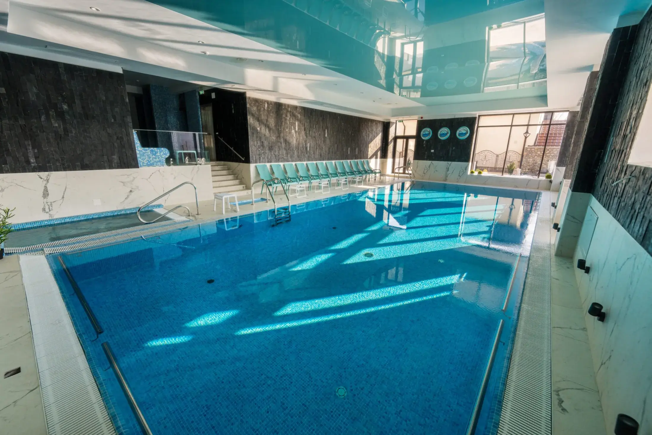 Piscina interioară văzută de pe margine, cu apa albastră și scări de acces