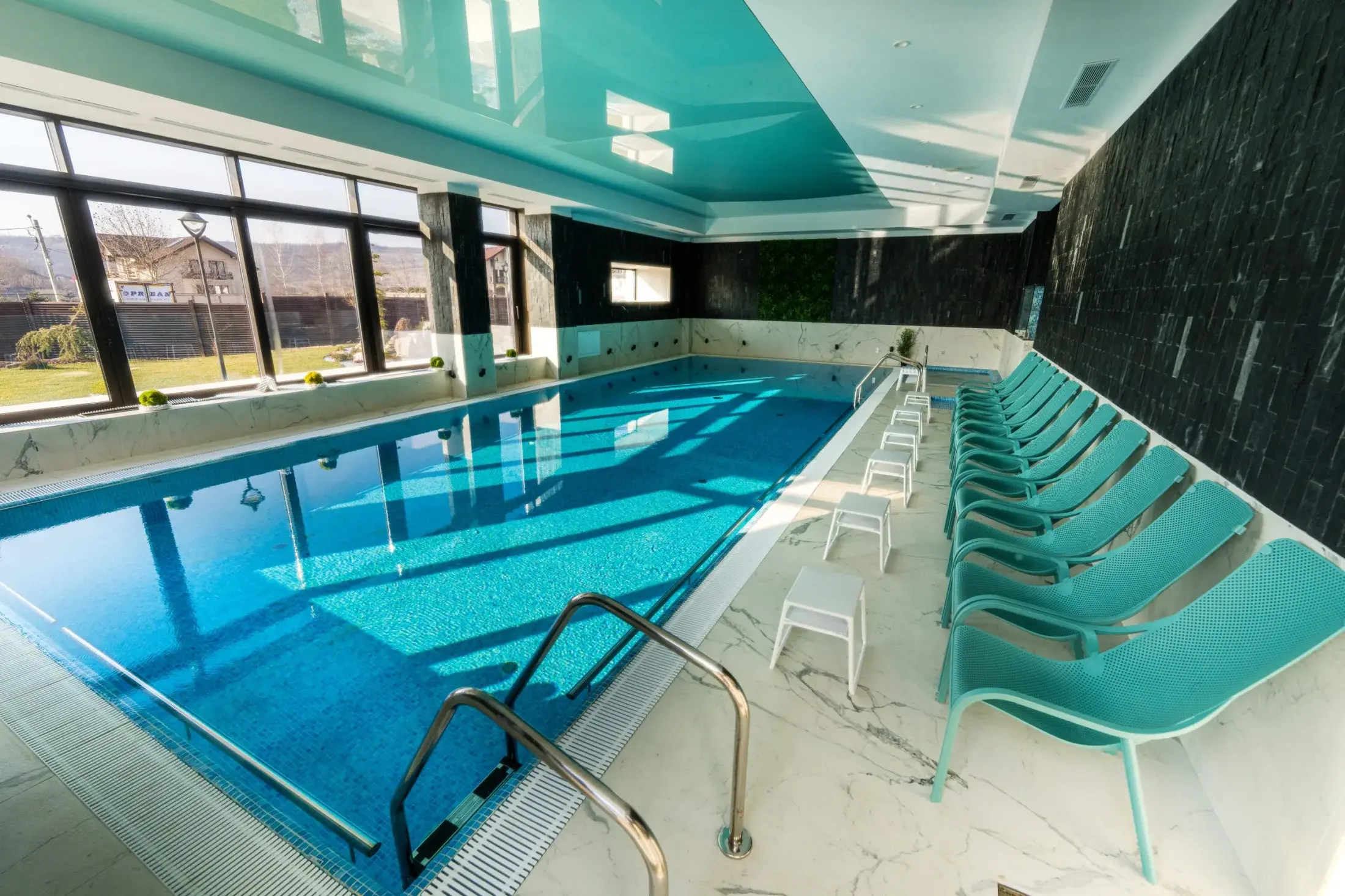 Margine a piscinei cu șir de șezlonguri turcoaz și ferestre mari