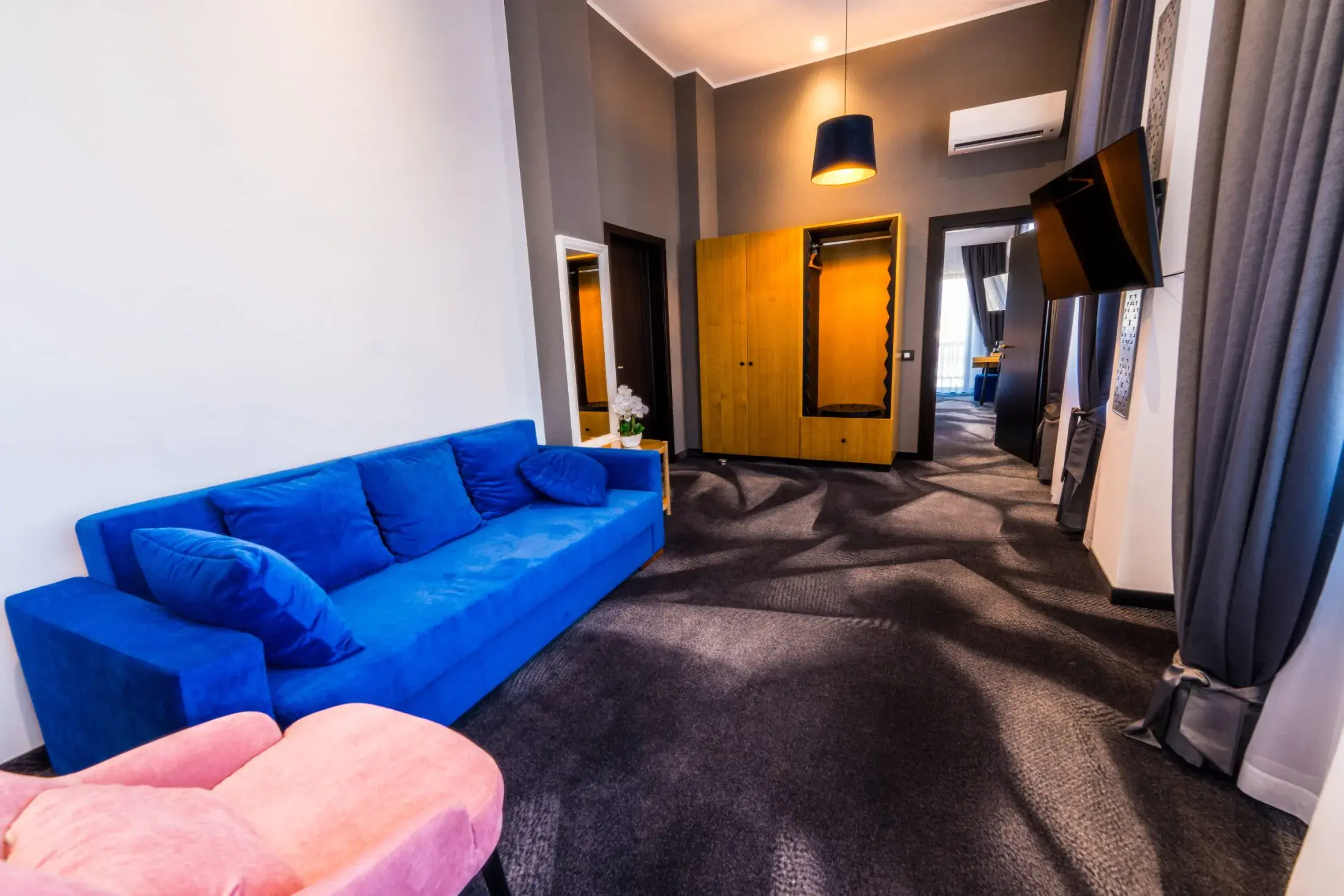 Zona de zi a apartamentului, cu canapea albastră, fotoliu roz și dulap din stejar