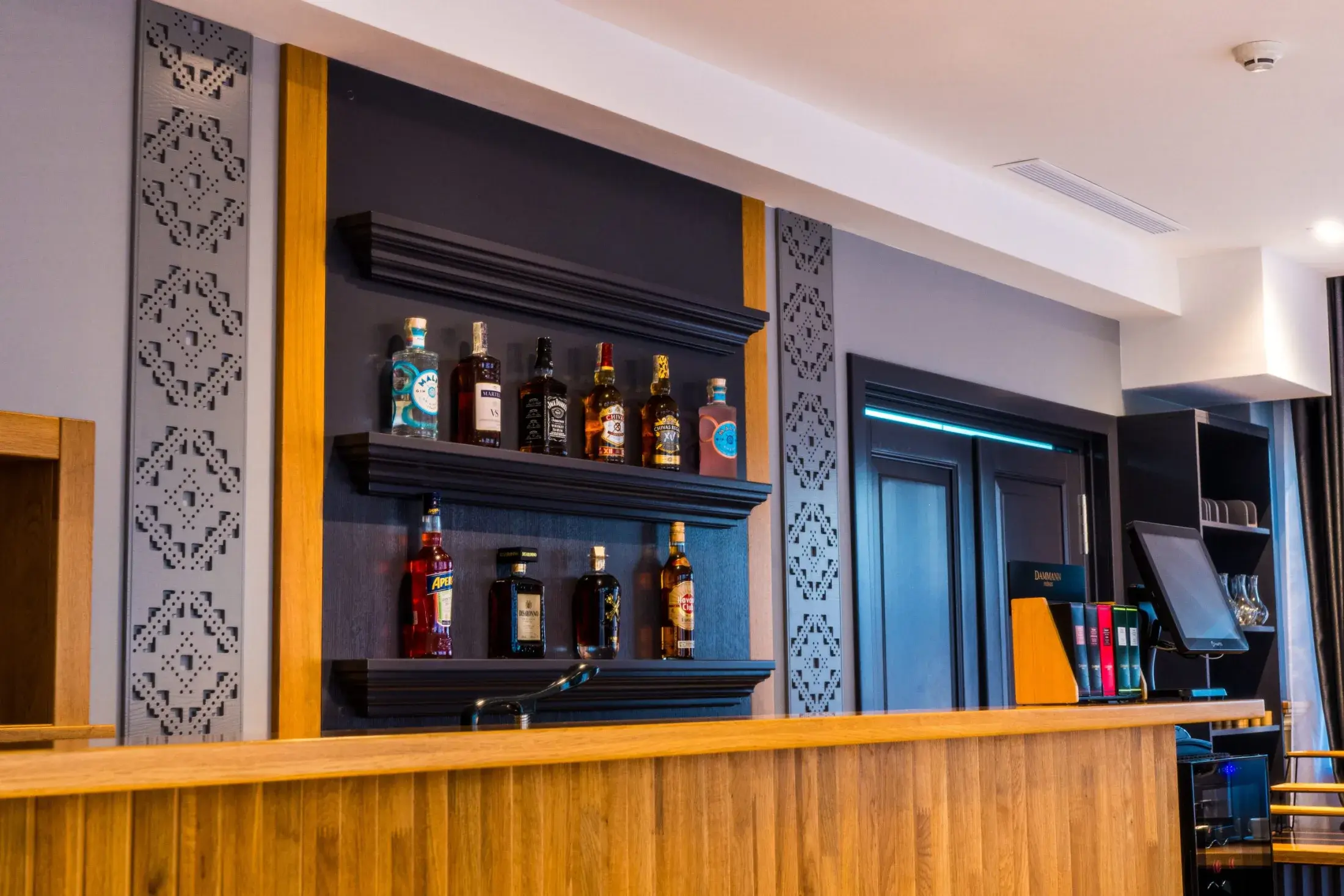 Barul restaurantului, cu sticle pe rafturi închise la culoare și panouri cu motive cioplite