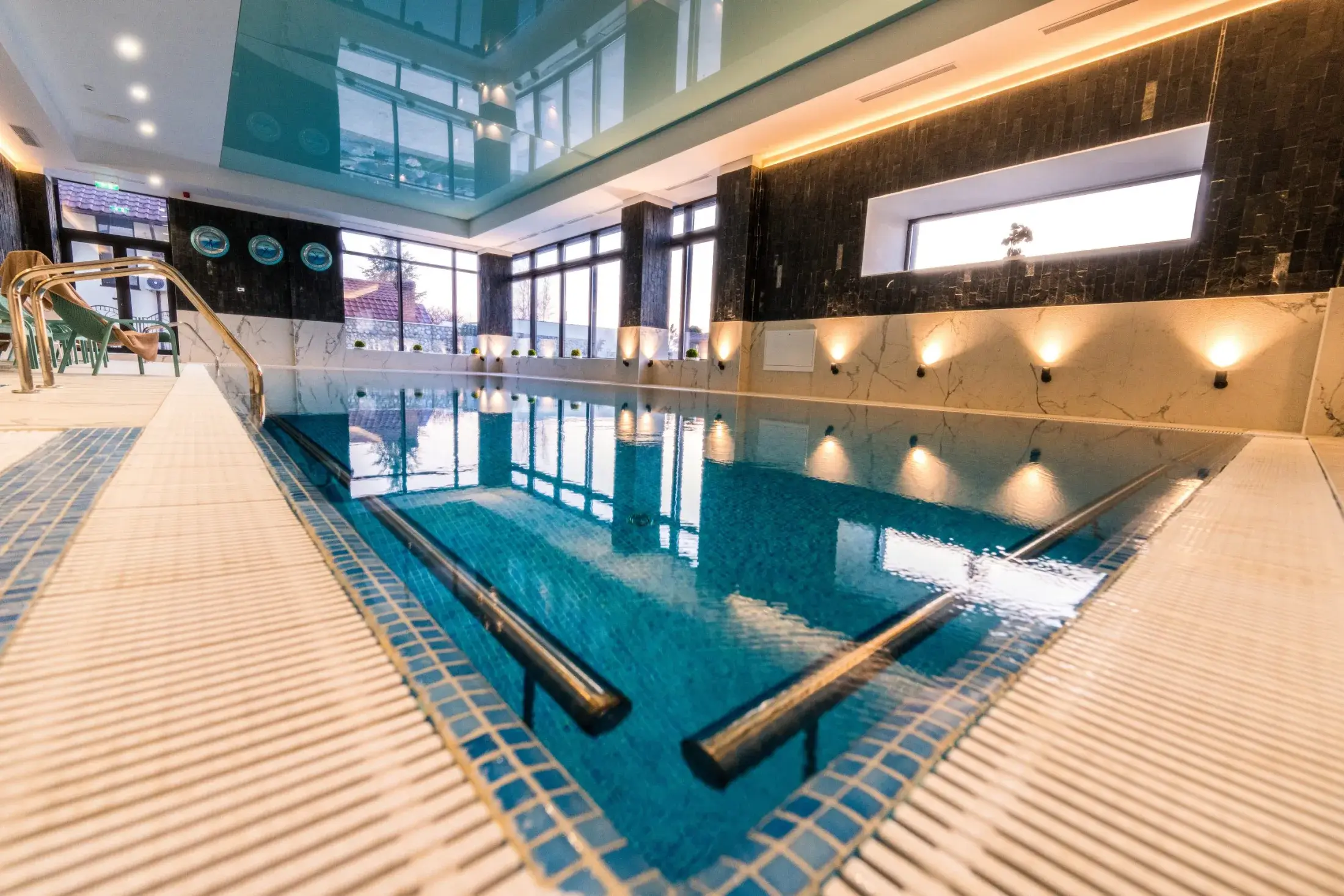 Piscina seara, cu lumini calde pe peretele de piatră neagră